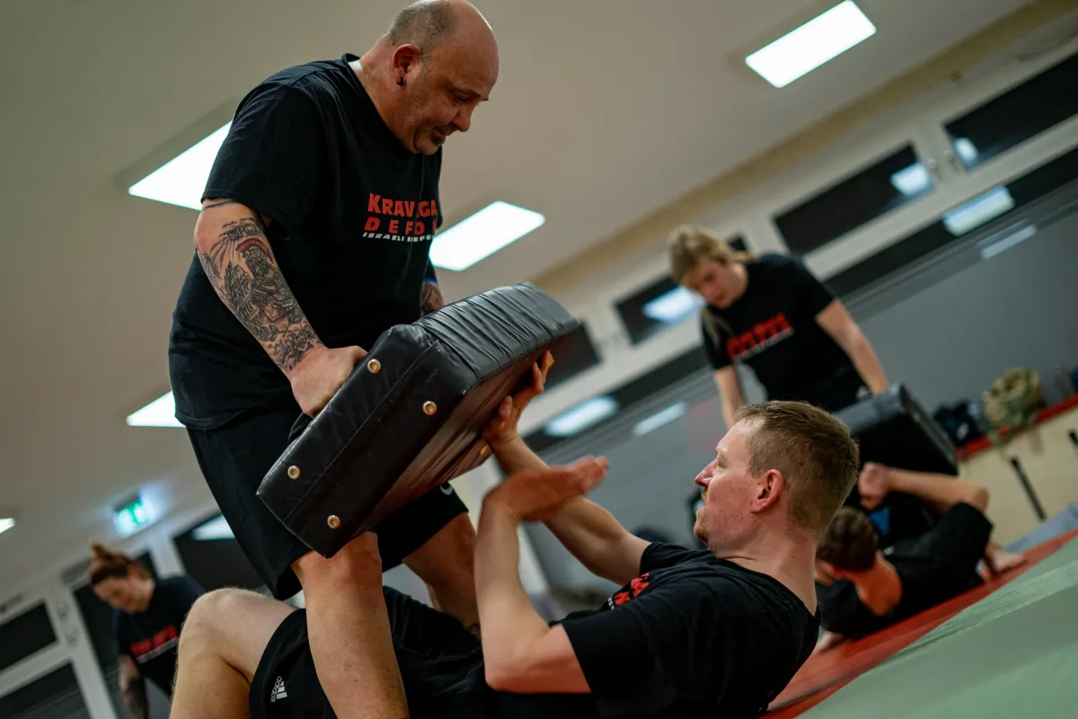 Krav-Maga-Training: Trainer hält ein Schlagpolster, ein Schüler trainiert am Boden