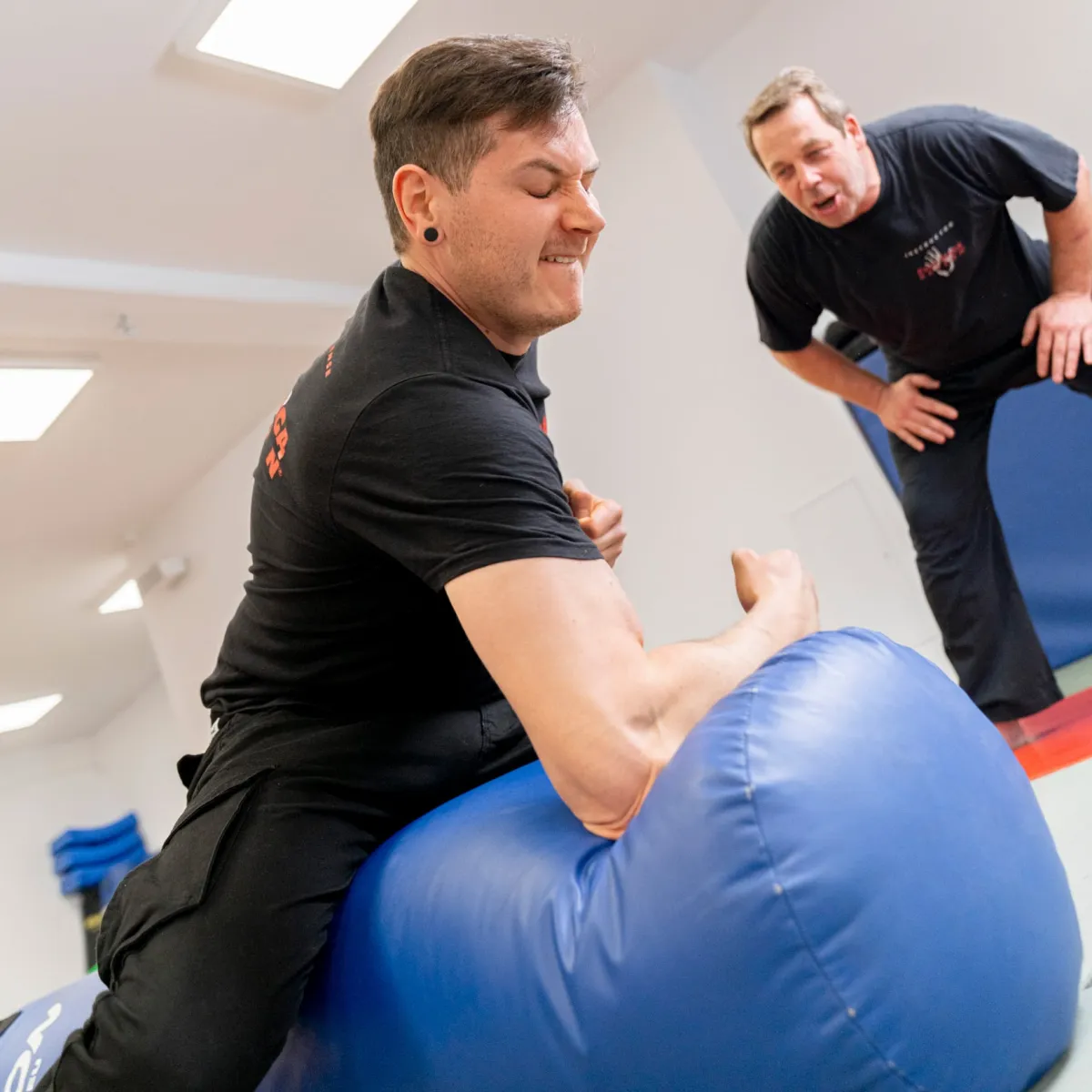 Schüler trainiert konzentriert an einem großen Schlagpolster, Trainer Markus Widmann feuert ihn an